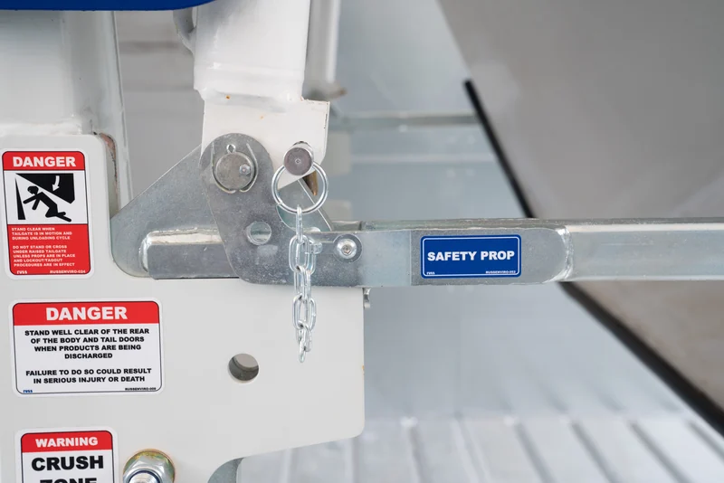 A safety prop and warning labels on a raised tailgate.